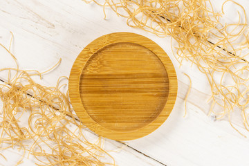 Lot of pieces of raw pasta noodles with empty bamboo plate in centre flatlay on white wood