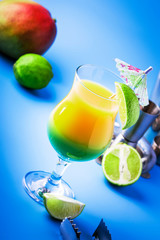 Double layer green yellow alcoholic cocktail with mango juice, rum, liqueur, lime and ice, blue background, copy cpase