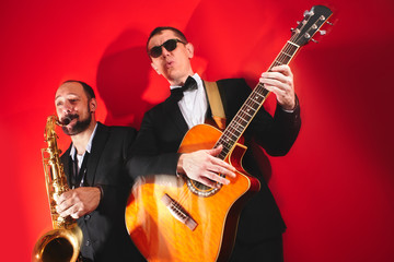 Group of two musicians, male jazz band, guitarist and saxophonist in classical costumes improvise...