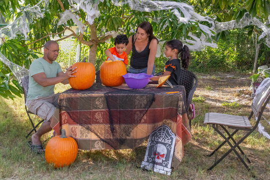 Halloween pumpkin carving is about working as a team in the backyard for this multiracial family. The mother, son, and daughter remove the insides of the pumpkin while the father designs the face.