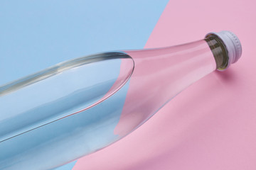 Glass bottle water on a bright pink and blue background close up