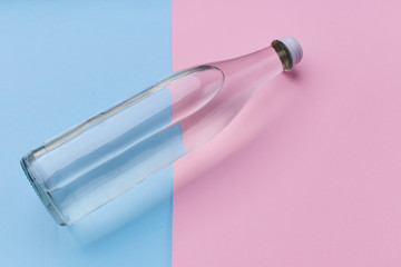 Glass bottle water on a bright pink and blue background close up