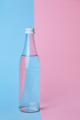 Glass bottle water on a bright pink and blue background close up