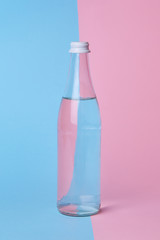 Glass bottle water on a bright pink and blue background close up