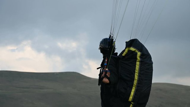 A male athlete paraglider raises a wing in an outdor against the backdrop of evening clouds but cannot fly. Failure while trying to take off