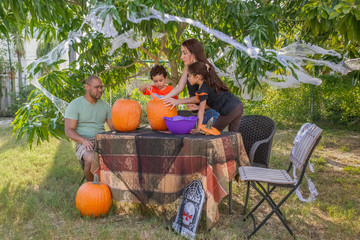 Obraz premium Halloween pumpkin carving is a family tradition gathered around the table in the backyard. The family works together creating the jack o lanterns to decorate for October 31st.
