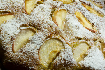 View of a freshly baked apple pie sprinkled with icing sugar, with apple slices