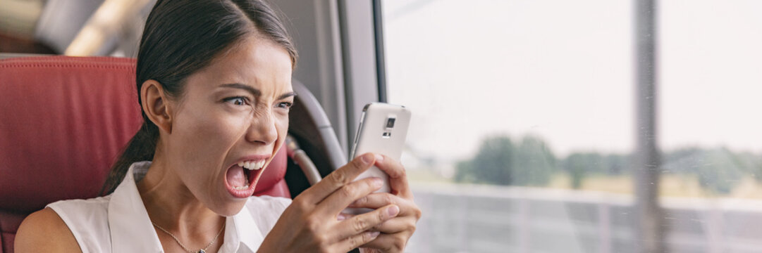 Angry crazy Asian woman upset at mobile phone problem not working or texting upset to somebody over smartphone 5g internet during work commute train ride panoramic banner.