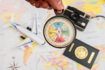 Woman hand holding a compass. A toy airplane, a vintage camera and a mexican passport appear out of focus on a map