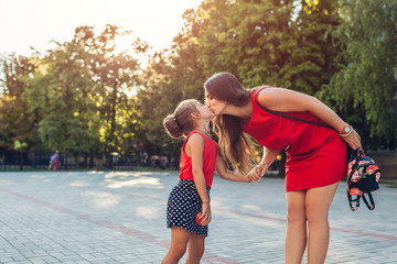 Happy mother meeting her daughters after classes outdoors primary school. Family kissing. Back to...