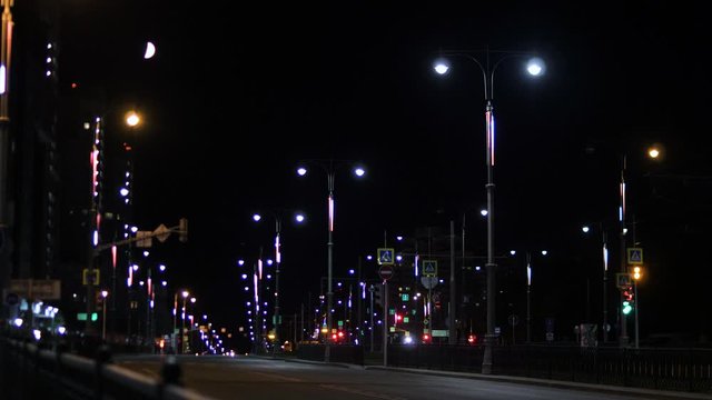 Lights of city at night on roadway. Stock footage. Night city is beautiful in neon lights on road. Summer night in city lit by dim light of lanterns on empty road