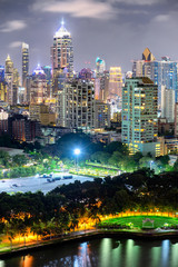 Fototapeta premium Cityscape, many modern building of midtown at night beautiful lighting, lake in park is foreground