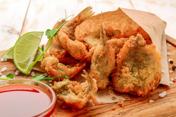 Fried crunchy anchovies on table with leaves salat. Paper background. Small fish in corn flour panning on the deep frying.