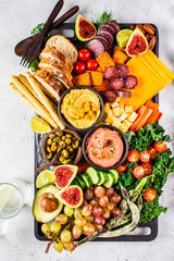 Meat and cheese appetizer platter. Sausage, cheese, hummus, vegetables, fruits and bread on black tray.