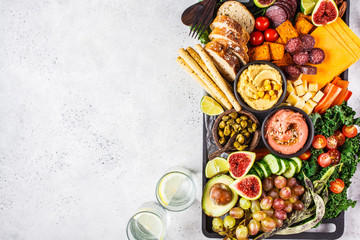 Meat and cheese appetizer platter. Sausage, cheese, hummus, vegetables, fruits and bread on black tray.