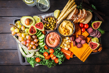 Meat and cheese appetizer platter. Sausage, cheese, hummus, vegetables, fruits and bread on black tray.