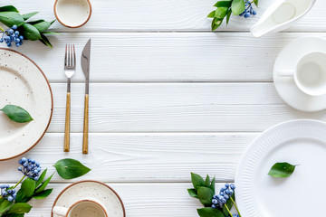 White plates and flowers for table setting frame on white wooden background top view mockup