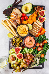 Vegan appetizer platter. Hummus, tofu, vegetables, fruits and bread on black tray.