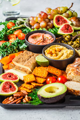 Vegan appetizer platter. Hummus, tofu, vegetables, fruits and bread on black tray.