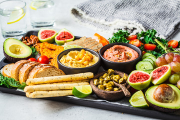 Vegan appetizer platter. Hummus, tofu, vegetables, fruits and bread on black tray, copy space.