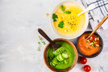 Three different vegetable cream soups in bowls on gray background. Corn, cucumber and gazpacho soups.