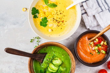 Three different vegetable cream soups in bowls on gray background. Corn, cucumber and gazpacho soups.