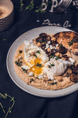 Poached eggs with runny egg yolk on a hummus with sautéed mushrooms, toasted bread anf herbs 
