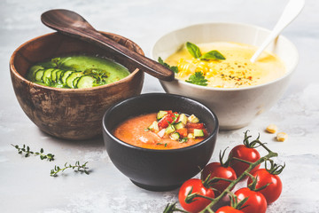Three different vegetable cream soups in bowls on gray background. Corn, cucumber and gazpacho soups.