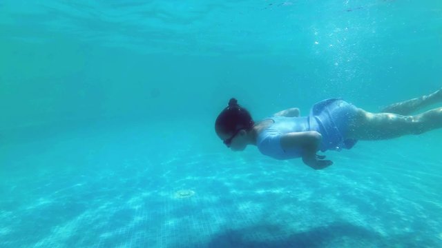 The little girl goes swimming and dives under the water to the bottom of the outdoor pool on a bright sunny day. Sport. Slow motion. Close-up. 4K.