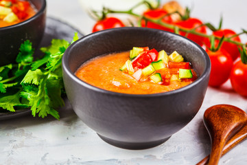 Traditional cold gazpacho tomato soup in black bowl on a gray background.