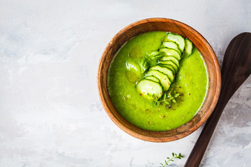 Vegan cold cucumber cream soup in wooden bowl on a gray background.