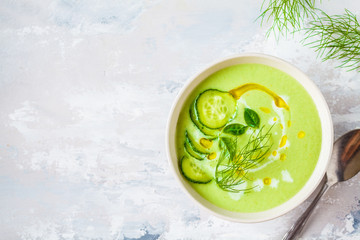 Vegan cold cucumber cream soup in white bowl on a gray background.