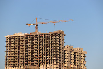 Construction crane and unfinished high-rise residential building on background of clear blue sky