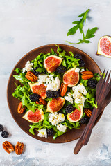 Salad with figs, feta cheese and blackberries in a wooden plate on white background, top view.