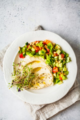 Hummus with vegetable salad and sprouts in white plate.