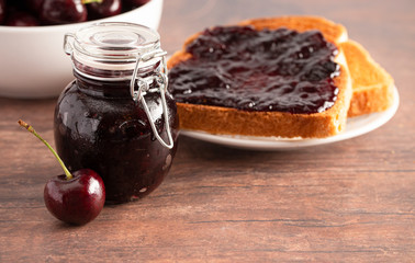 Jar of Homemdae Cherry Jam on a Rustic Wooden Table