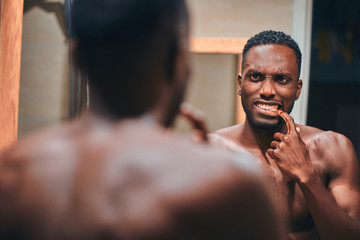 Handsome african man is checking his teeth in the bathroom while see himself in the mirror.