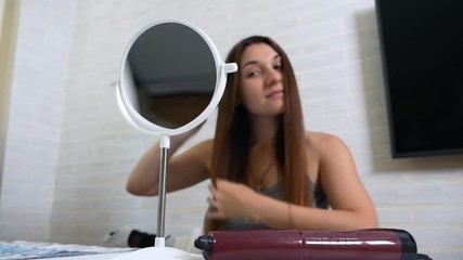 Young pretty woman combing her hair in front of the mirror
