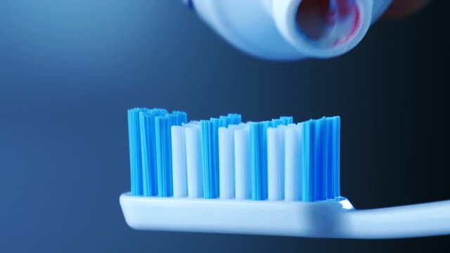 Dental Health - Squeezing toothpaste with colorful stripes from a tube onto a toothbrush.