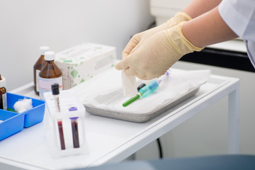 gloved laboratory assistant preparing for blood sampling against a background of blood tubes