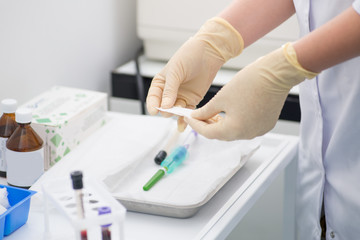 gloved laboratory assistant preparing for blood sampling against a background of blood tubes