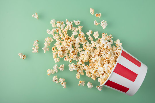 Overturned striped paper cup with delicious fresh popcorn on green background. The concept of entertainment.