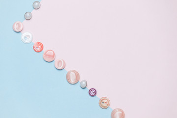 Buttons, accessories for sewing and needlework on pastel pink and blue background. Copy space, flat lay.