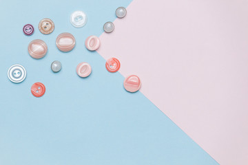 Buttons, accessories for sewing and needlework on pastel pink and blue background. Copy space, flat lay.