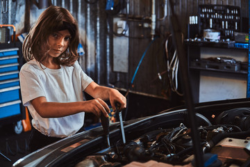 Fototapeta na wymiar Little pretty girls is dreaming to be at auto technicial, she is trying to fix broken car.