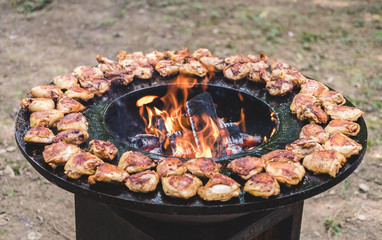 Round barbecue grill with open fire inside. Meals for summer picnic are being prepared: chicken pieces.
