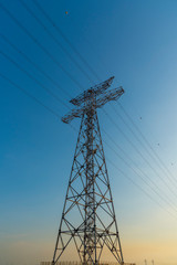 a full-length vertical shot of a power transmission tower on background of blue sky