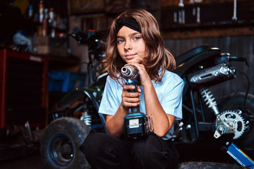Fototapeta na wymiar Pensive beautivul kid is posing with screwdraiver at auto service workshop.