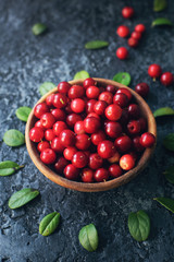 Raw organic fresh cowberry or lingonberry in wooden bowl on dark stone table