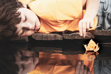 yellow autumn leaf ship in children hand, boy play in water pond